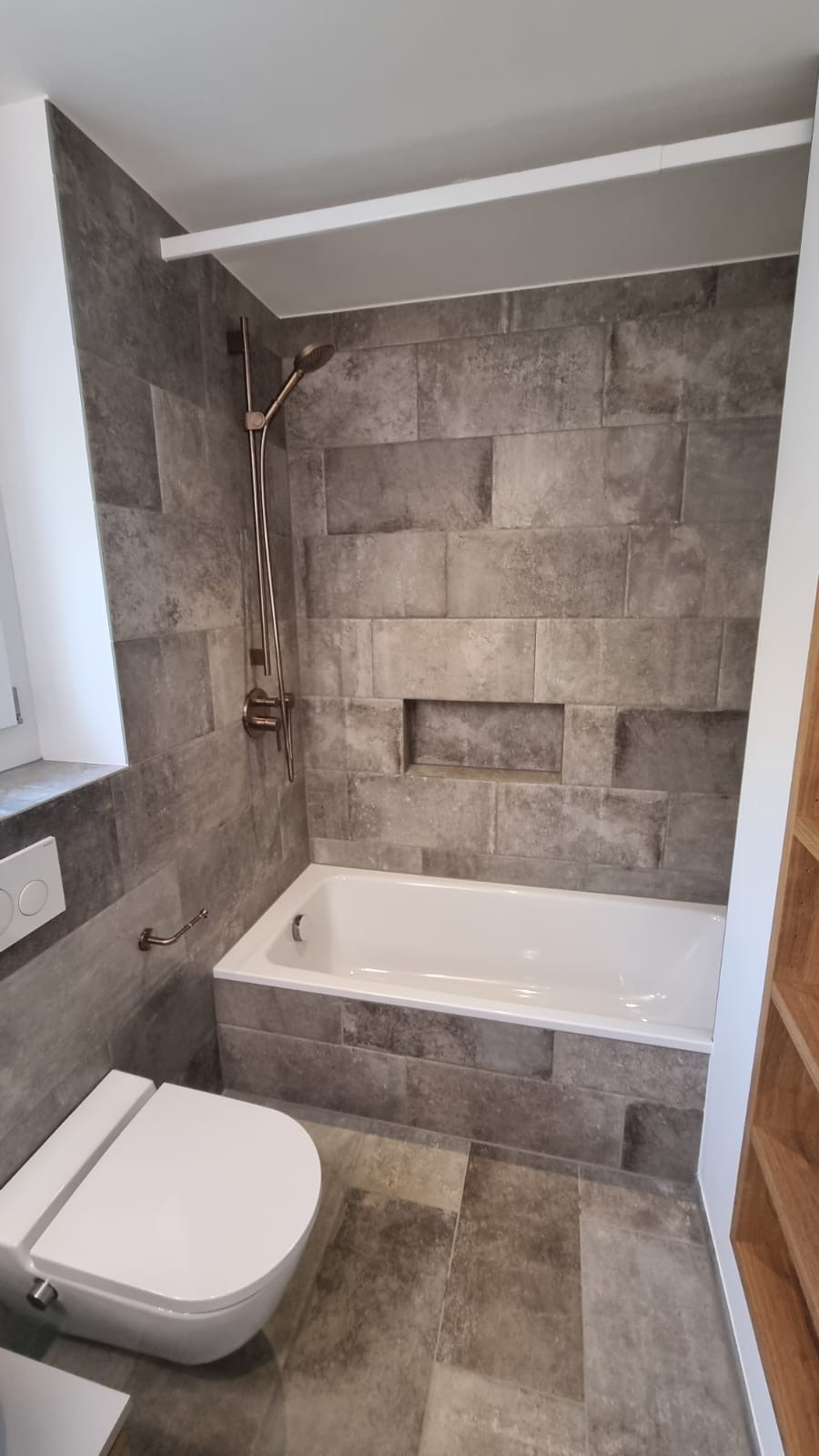 Gefliester Badewannenbereich mit Wandplatten in Steinoptik und eingelassener Nische