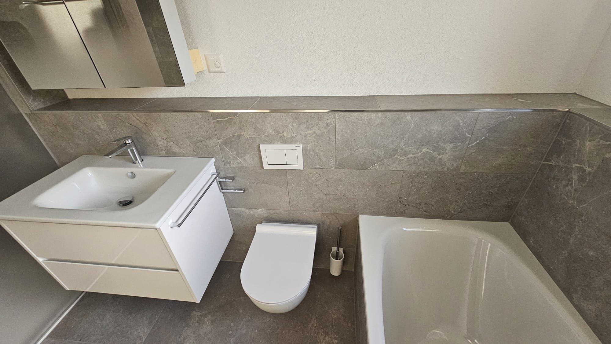 Bad mit Badewanne, Waschtisch und grauen Wandplatten