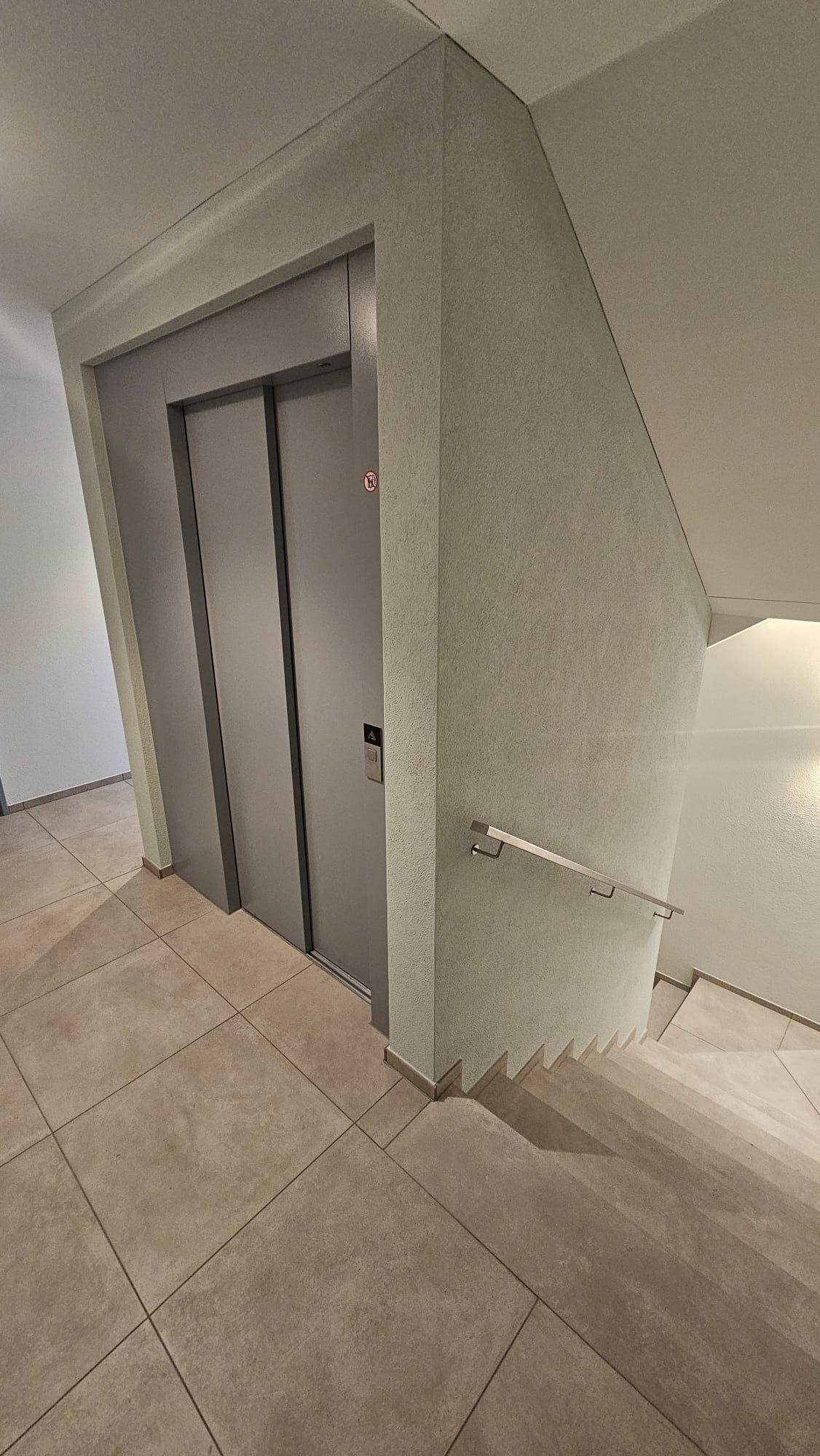 Treppenhaus mit Lift, Wand und Boden mit grossformatigen hellen Fliesen